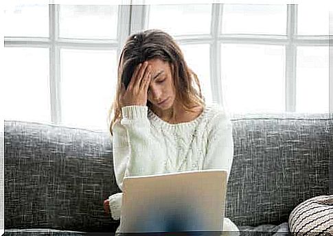 A woman with her hand to her head is sitting behind a laptop